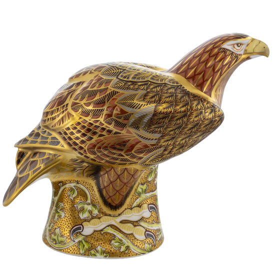 A decorative ceramic eagle figurine perched on a patterned pedestal, featuring intricate gold, brown, and cream detailing against a plain white background.